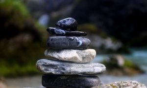 black and white rocks stacked up in a pile on top of a larger grey rock near an aqua stream with green moss forest trees, very moody, natural fresh clean feeling