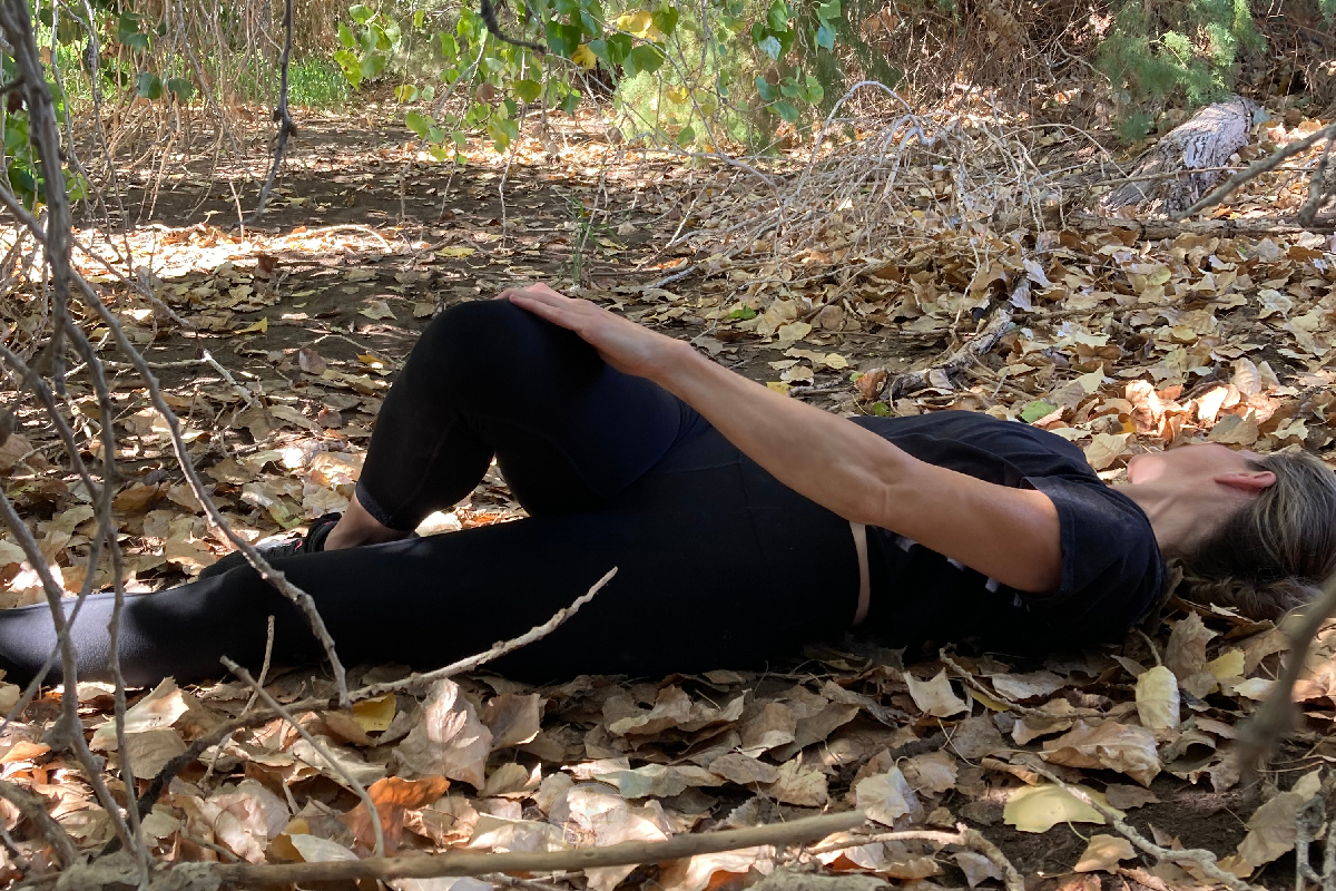 rotating knee with opposite hand woman stretches in the woods black workout leggings and croptop blond hair pulled back face turned away